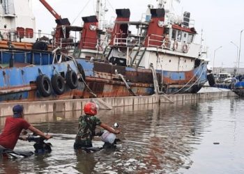 TERENDAM: Dua warga menuntun sepeda motornya saat melintas di kawasan Pelabuhan Tanjung Emas, Kota Semarang, Senin (23/5) yang dilanda banjir rob dengan ketinggian 125-200 cm.