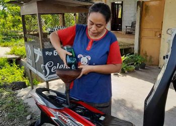 MELAYANI: Sumarni, penjual bensin eceran sedang melayani pembeli. (Lilik Yuliantoro/Harianmuria.com)