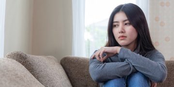 Unhappy asian pretty young woman siting alone on couch with feeling sadness