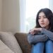 Unhappy asian pretty young woman siting alone on couch with feeling sadness